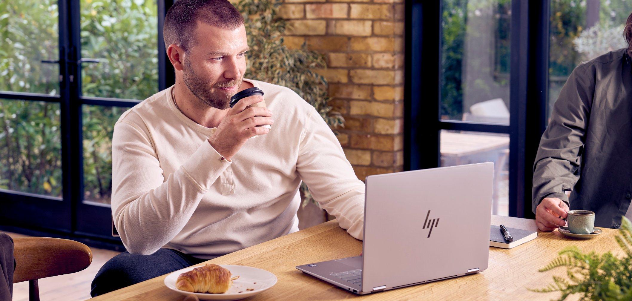 a man sitting at a table with a laptop and a cup of coffee