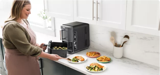 A woman preparing food in a kitchen with a toaster oven
