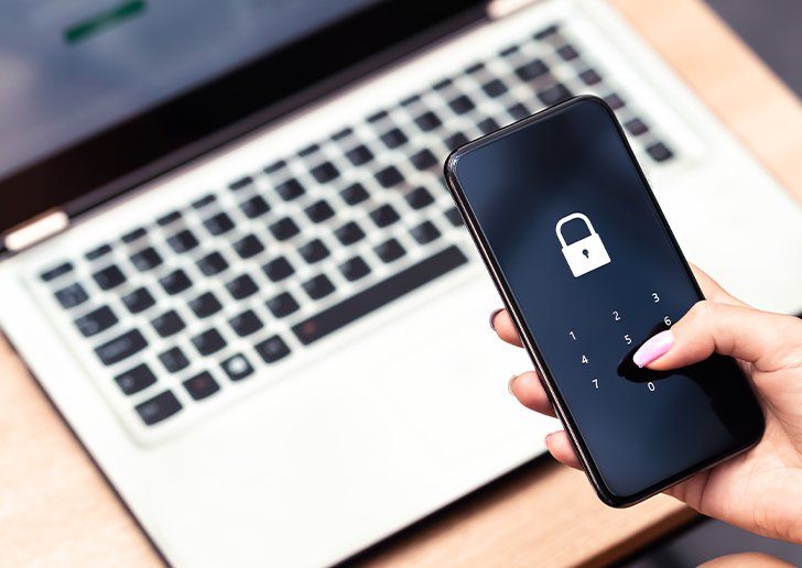 A person holding a phone whilst using a laptop, the phone has a lock icon on the screen