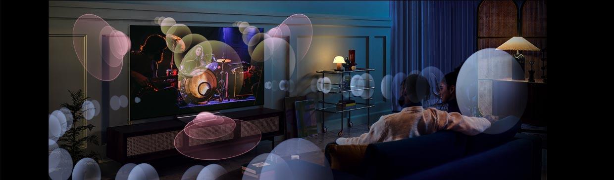 A couple watch TV on the sofa with illustrative shapes showing immersive surround sound 