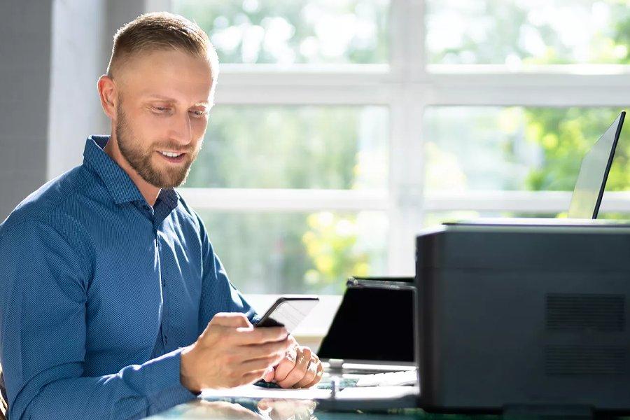 A man holding a smart phone whilst sitting at a desk