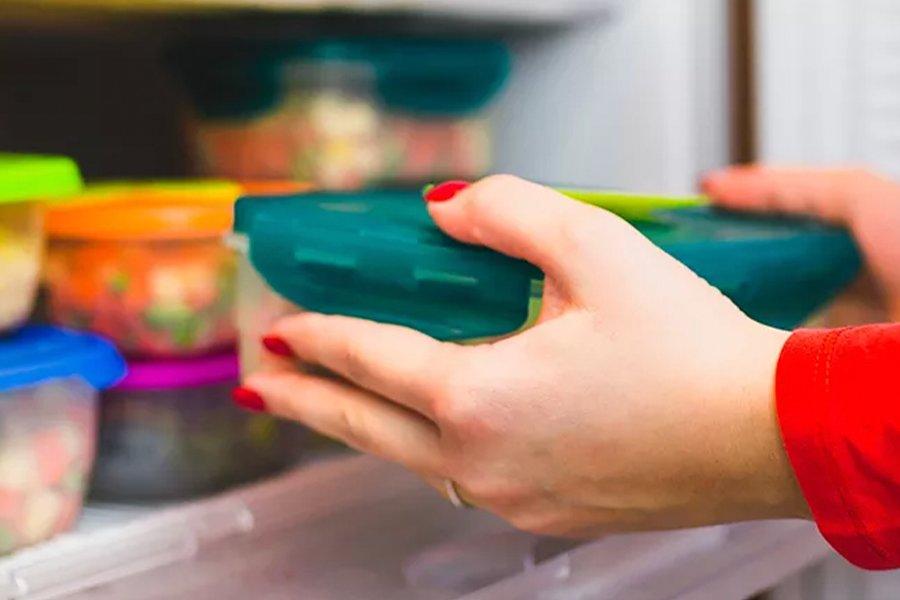 A pair of hands putting a tupperware into a freezer