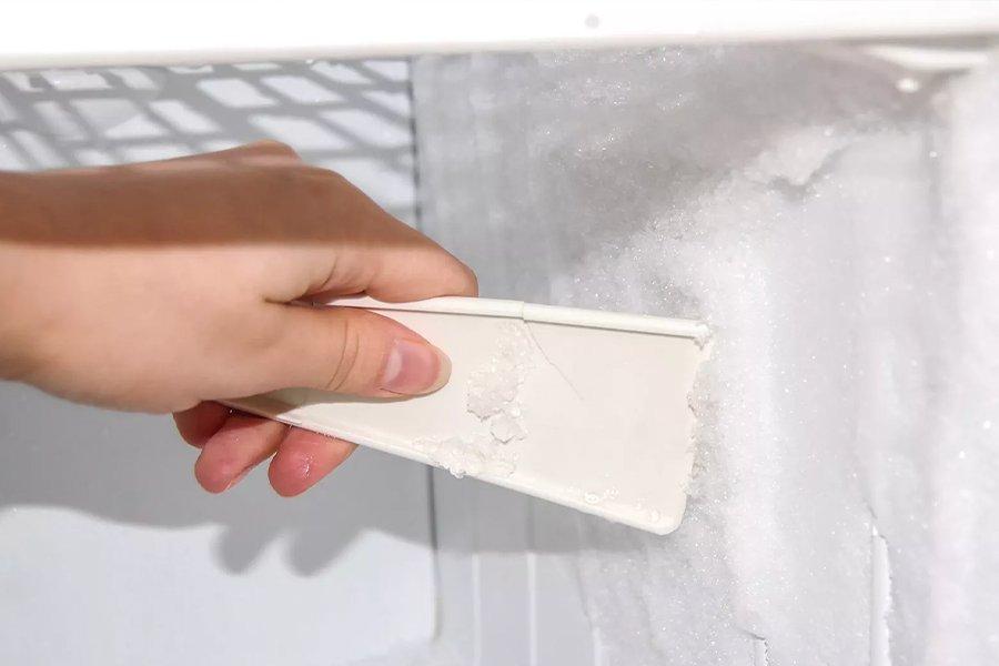 A hand holding a scraper inside a freezer covered in ice