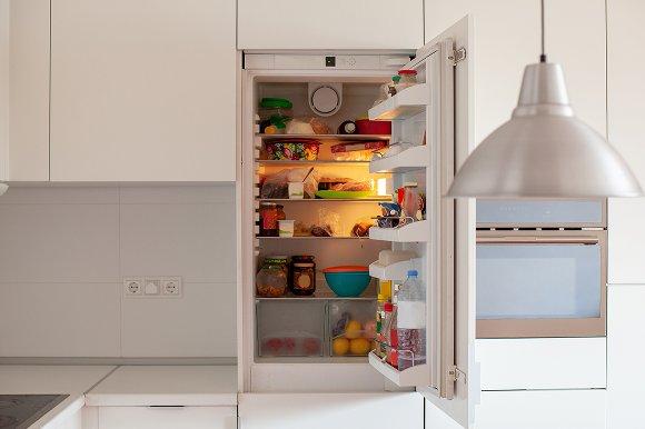 An integrated fridge full of food open in a kitchen