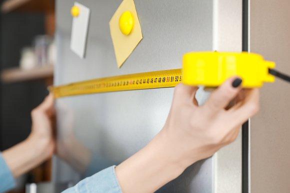 A person measuring a fridge with a tape measure