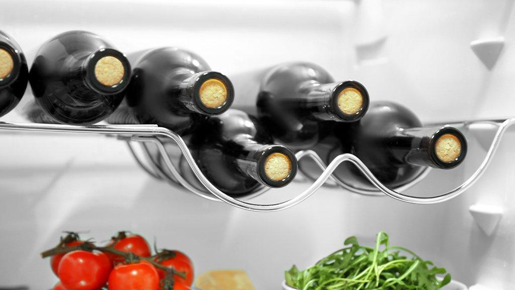 A wine rack in a fridge with wine stacked in it