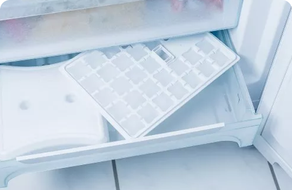 A freezer with a drawer open, an ice cube tray is lying on top of it