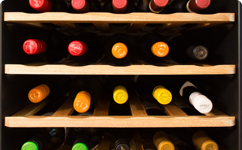 The ends of lots of wine bottles on shelves