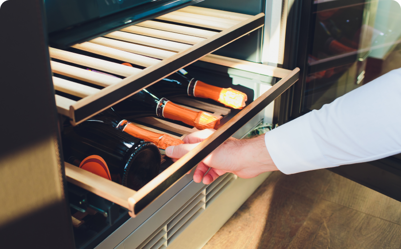 A hand reaching into a wine cooler with a shelf rolled out