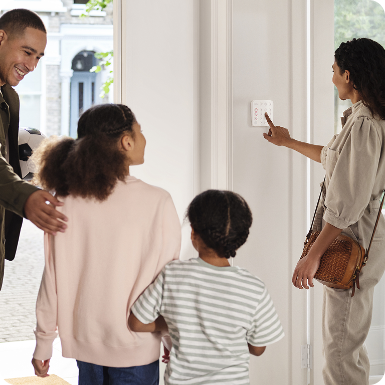 A family is standing in front of a RIng security panel whilst mum presses the buttons