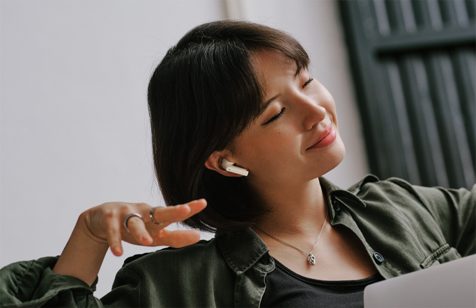 A woman smiling with her eyes closed wearing a pair of white earbuds