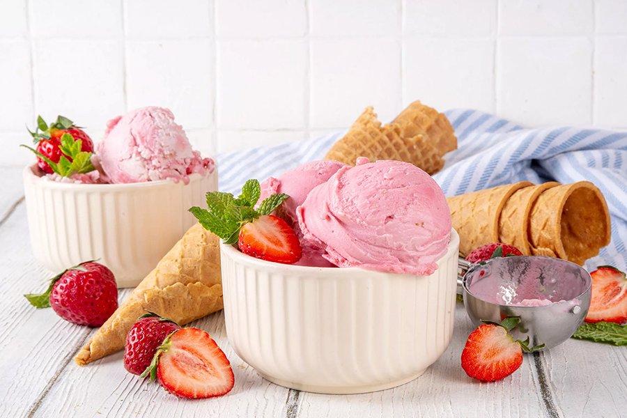 Two bowls of pink ice cream surrounded by cones and strawberries