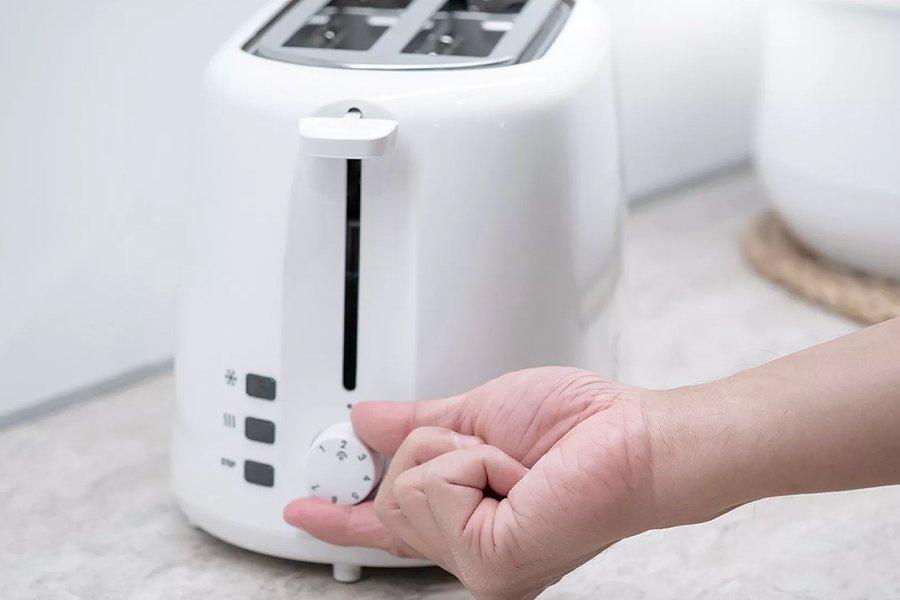 A person moving the dial on a white toaster