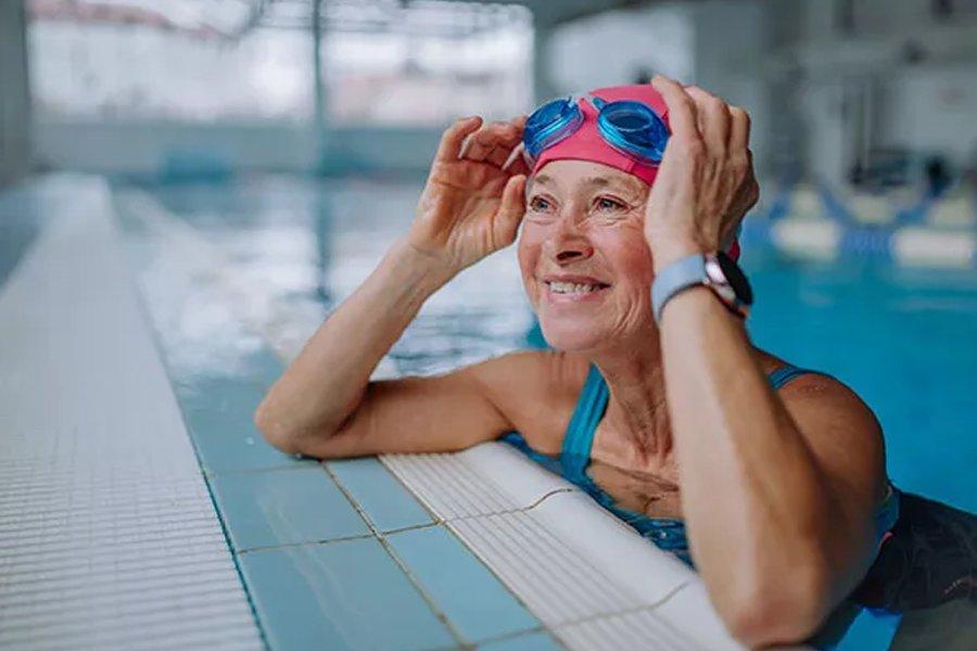 A woman in a swimming pool leaning on the edge wearing a smart watch