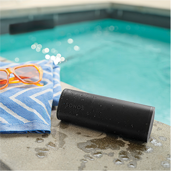 A black portable speaker next to a towel and sunglasses, next to a pool