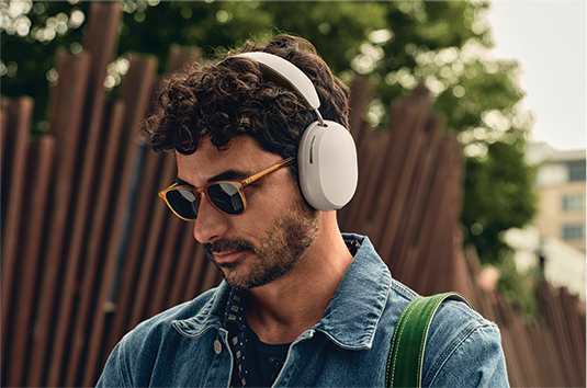 A man wearing sunglasses has a white pair of over-ear headphones on