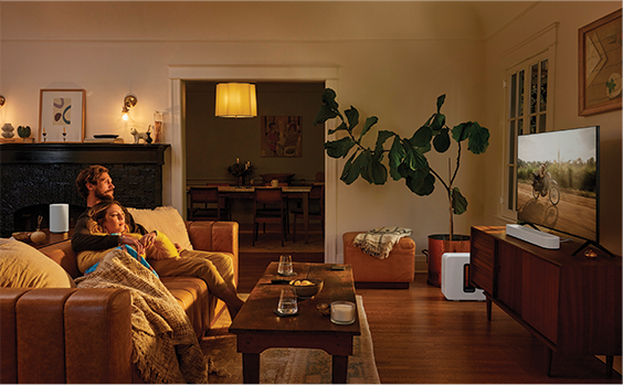 A couple on a sofa in a dimly lit room, watching TV with a soundbar next to it