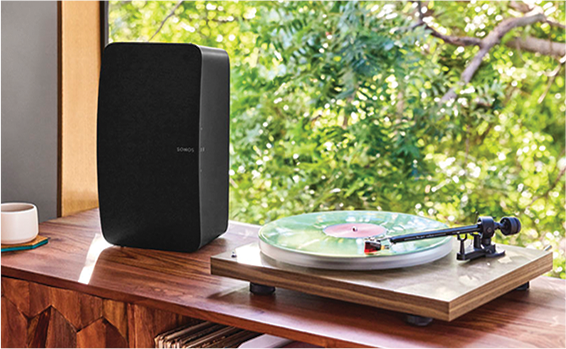 A black speaker is on a shelf in front of a window next to a record player