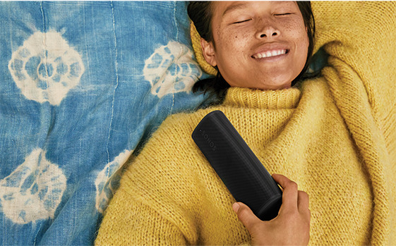 A woman lying down with her eyes closed with a speaker on her chest