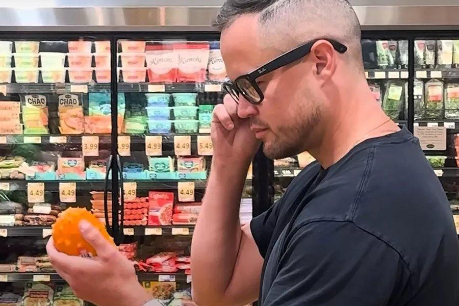 a man wearing glasses in a shop holding and looking at some fruit