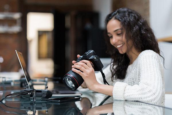 a woman holding a camera and looking at a laptop