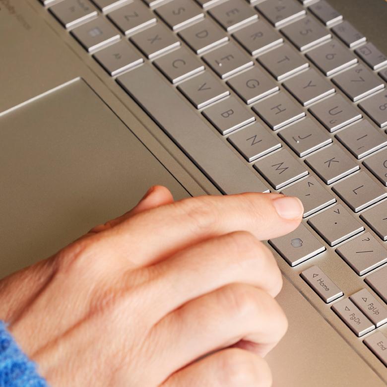 a person typing on a laptop keyboard with a blue sweater