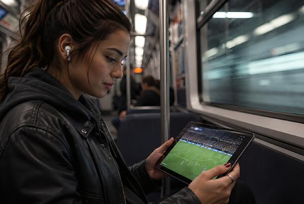 a woman sitting on a train holding a tablet with a soccer game on it