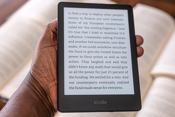a person holding a kindle in front of a stack of books