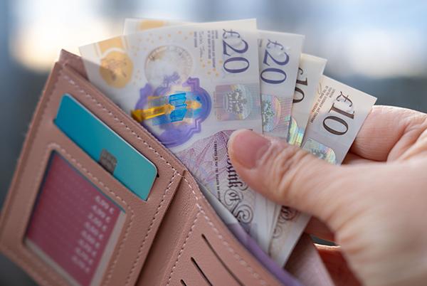 a person holding a pink wallet with some money in it