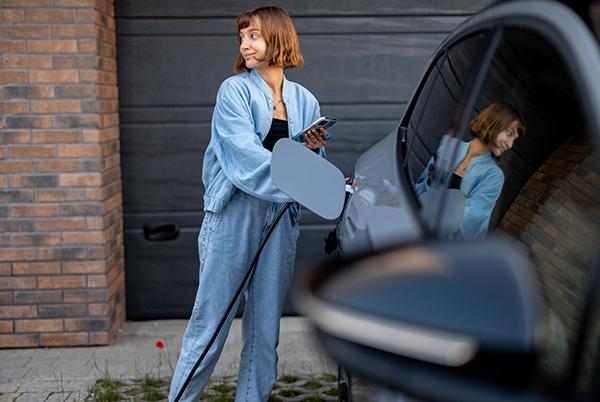 a woman in blue jeans standing next to a car with a charger