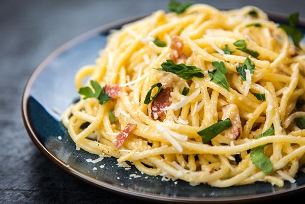 a plate of pasta with bacon and parsley on a blue plate