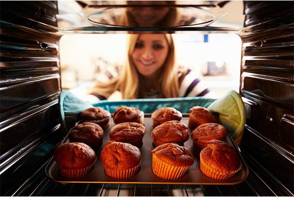 a woman in a kitchen looking at a tray of muffins