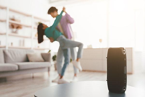 a couple dancing in a living room with a speaker on a table