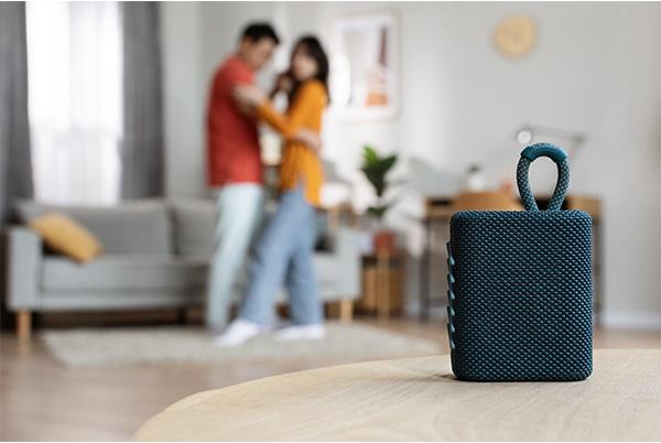 a couple dancing in a living room with a blue speaker in the background