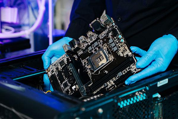 a person in blue gloves holding a motherboard in a computer case