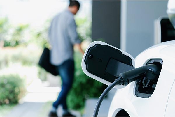 a man is walking towards a white car with an electric plug