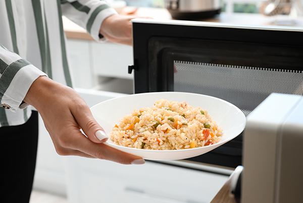 a person holding a bowl of rice in front of an open microwave