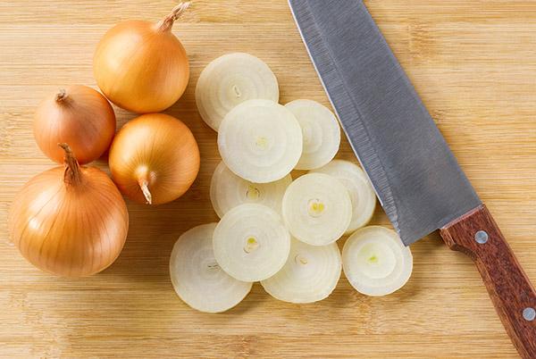 a knife and onions on a cutting board with a few onions