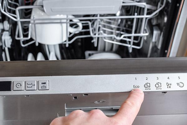 a person pointing to a button on a dishwasher in a kitchen