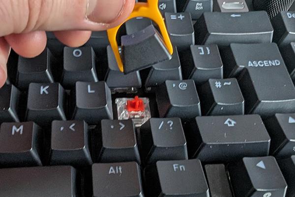 a person holding a yellow tool to remove a key from a keyboard