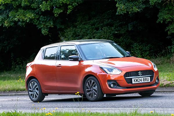 a small orange hybrid car driving down a road next to a tree