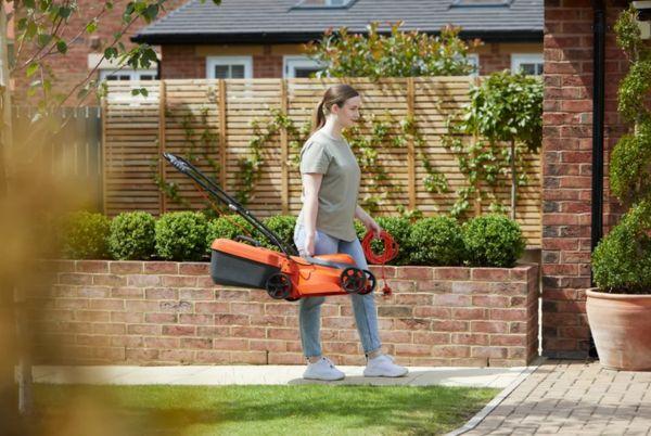 a woman walking with a Flymo SimpliCompact lawn mower in a garden