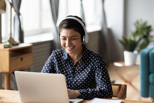 a woman wearing over ear headphones sitting at a desk with a laptop