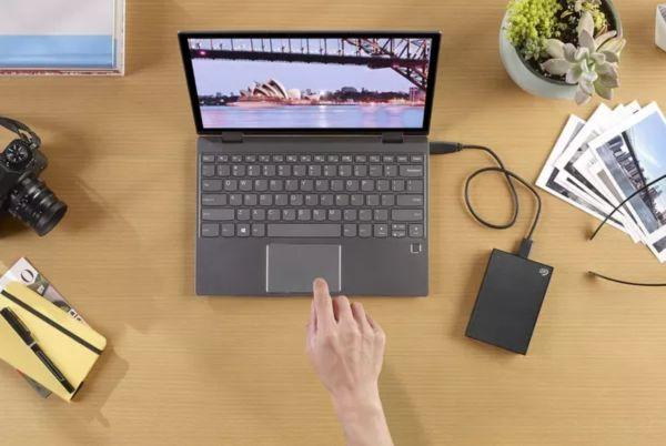 a person is touching a laptop on a desk with an external harddrive plugged in