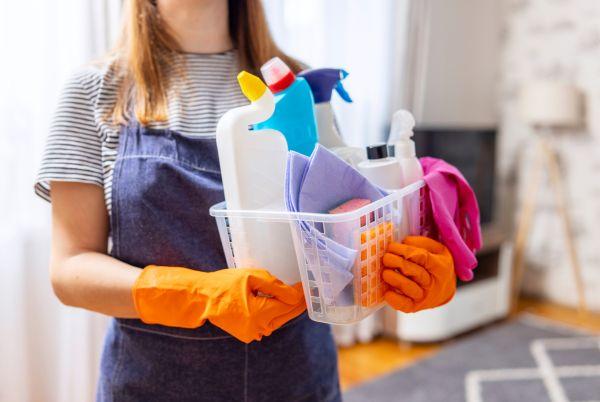 a woman holding a basket full of cleaning supplies