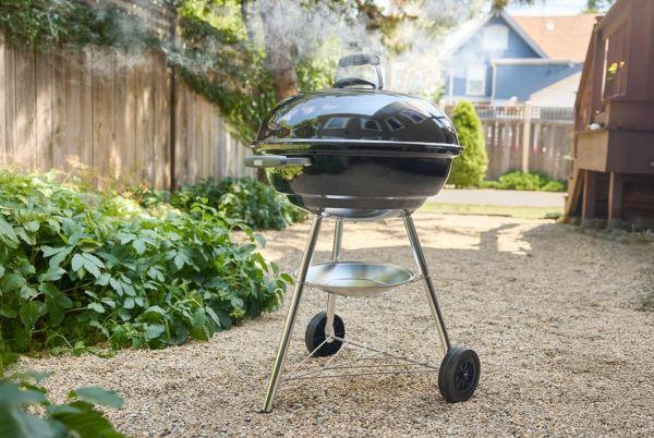 a Weber 57cm kettle BBQ sitting on a gravel driveway in a backyard