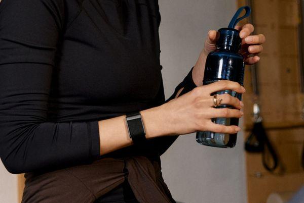 a woman in a black shirt holding a water bottle, wearing a WHOOP fitness tracker