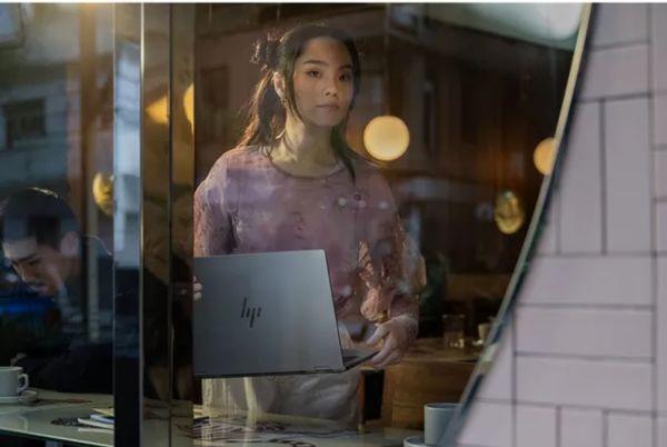 a woman is looking at a laptop through a window
