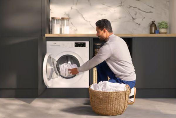 a man is putting a load of laundry into a Beko Pro Integrated washing machine