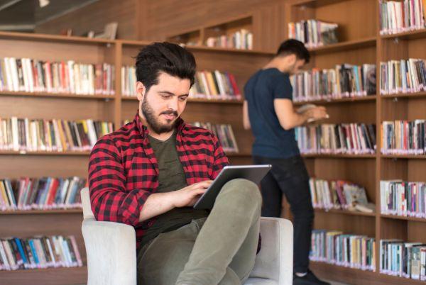 a man sitting in a chair in a library with a tablet